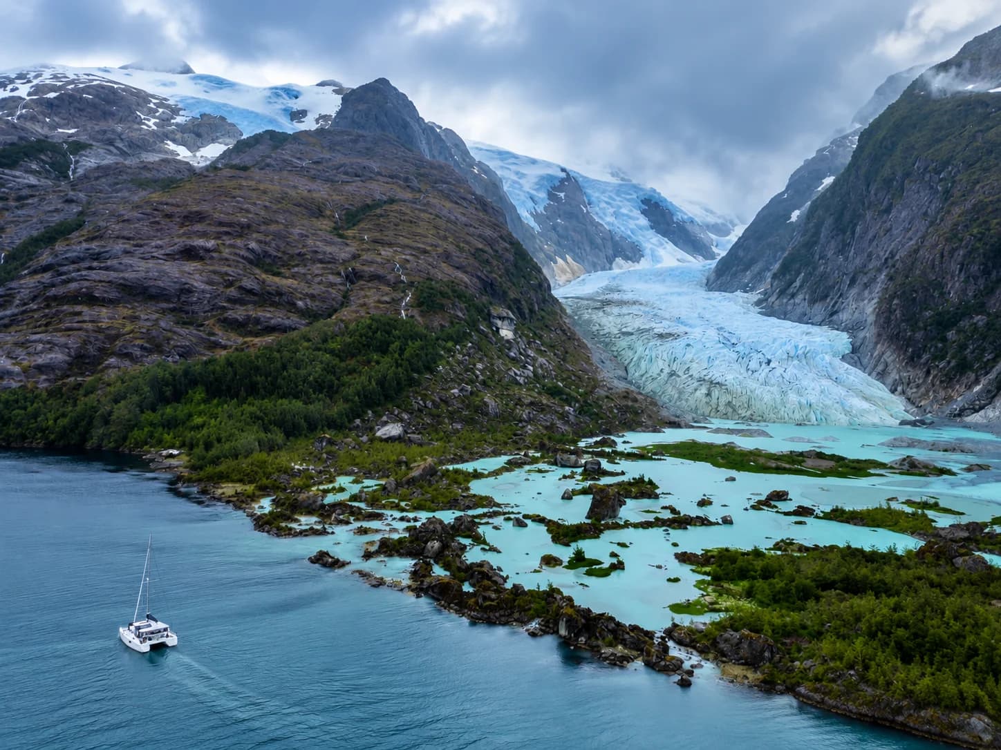 Vista aérea de un catamarán fondeado junto a un glaciar en los canales de Magallanes