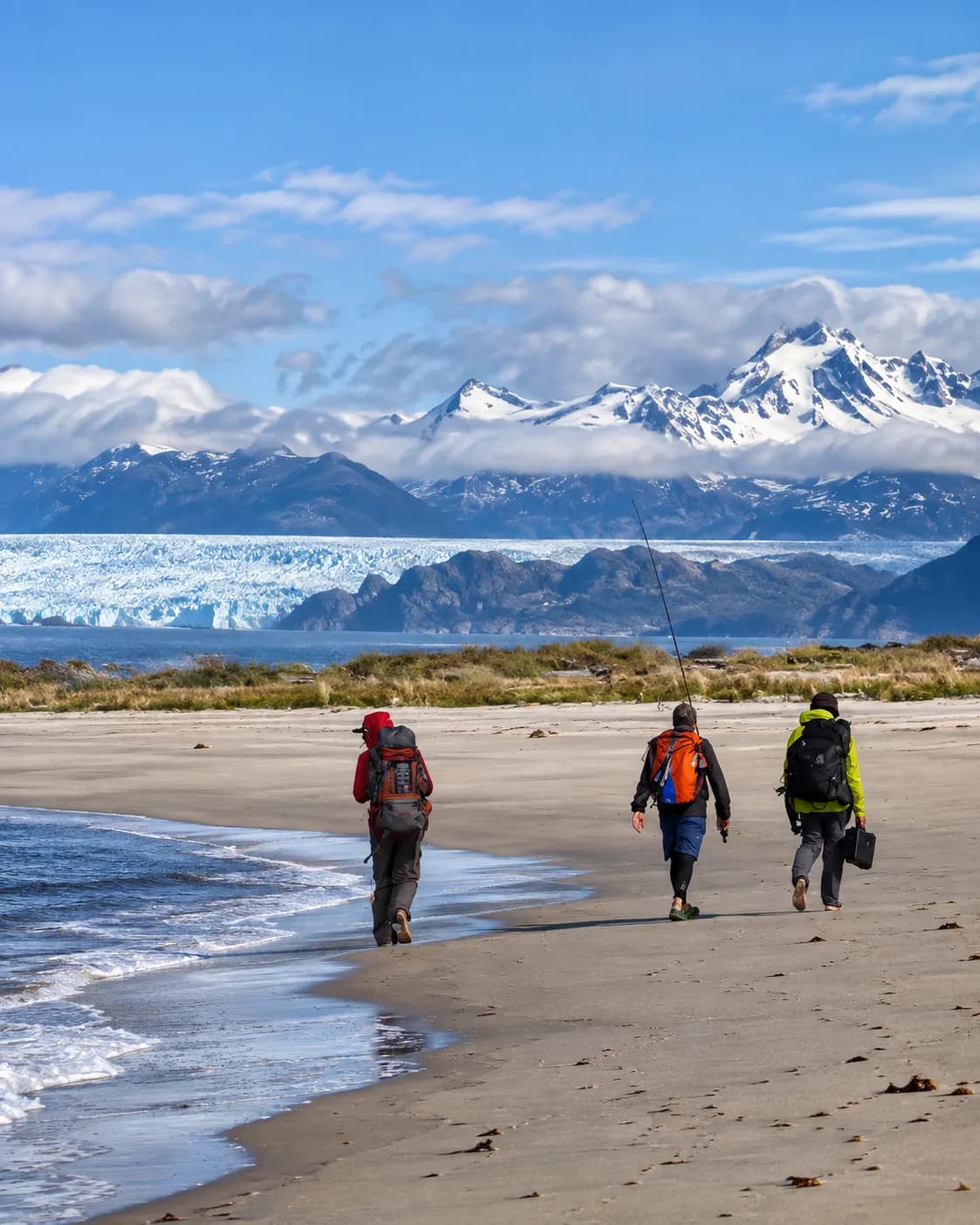 Tres personas caminando por una playa frente a un glaciar y montañas nevadas