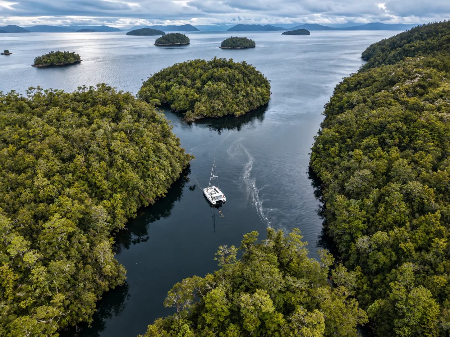 Vista aérea de un catamarán fondeado entre islas boscosas de un canal patagónico