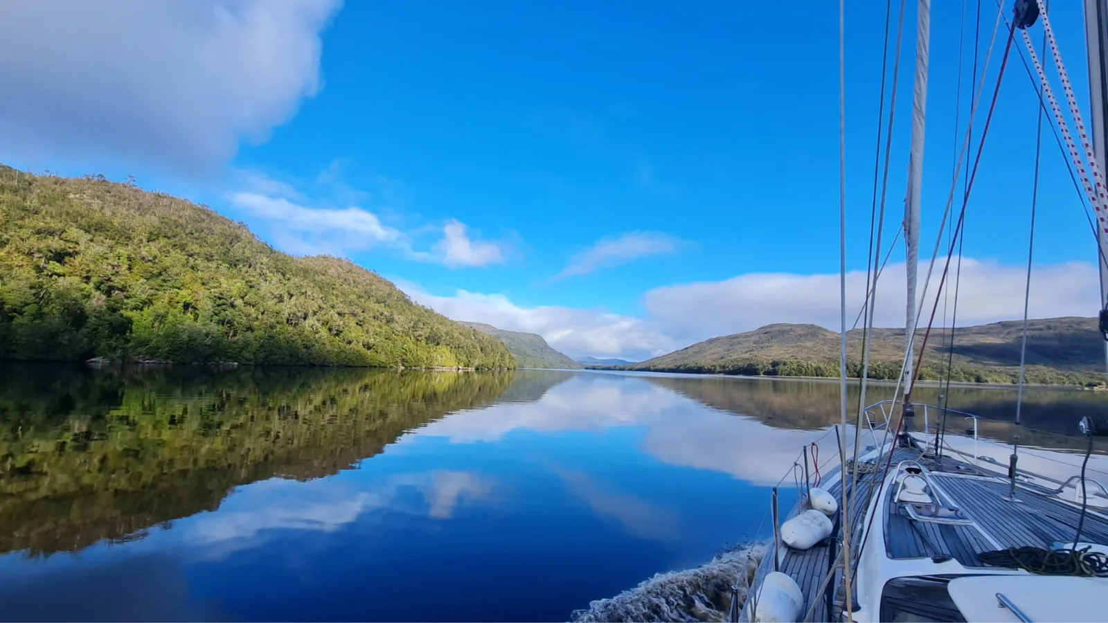 Velero navegando un canal patagónico entre cerros boscosos