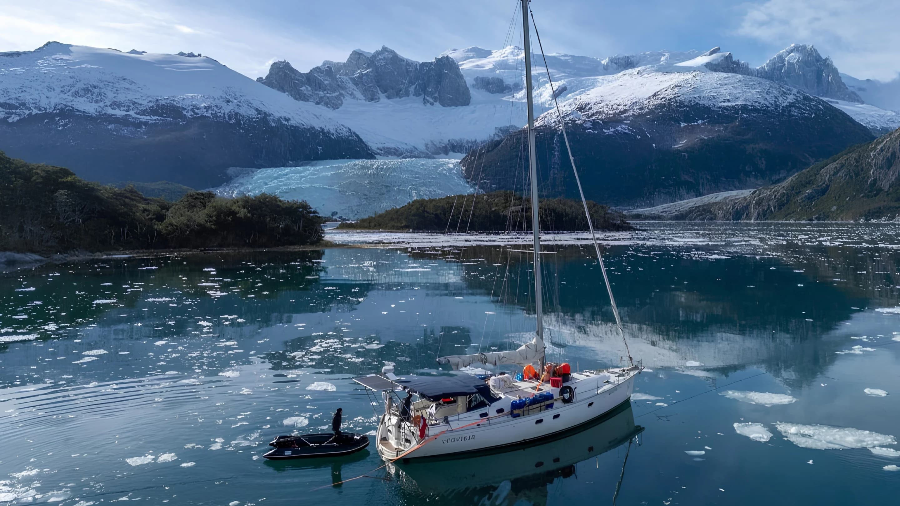 Velero navegando frente a un glaciar en un fiordo patagónico