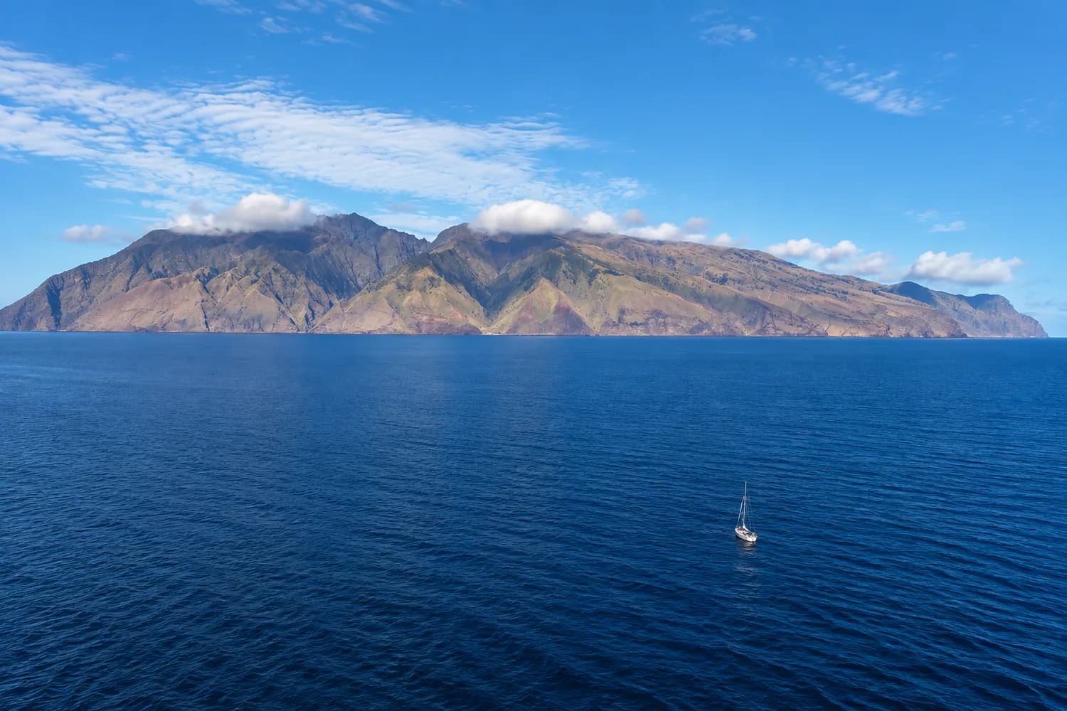 Costa montañosa y escarpada de la isla Alejandro Selkirk vista desde el mar, con un velero solitario