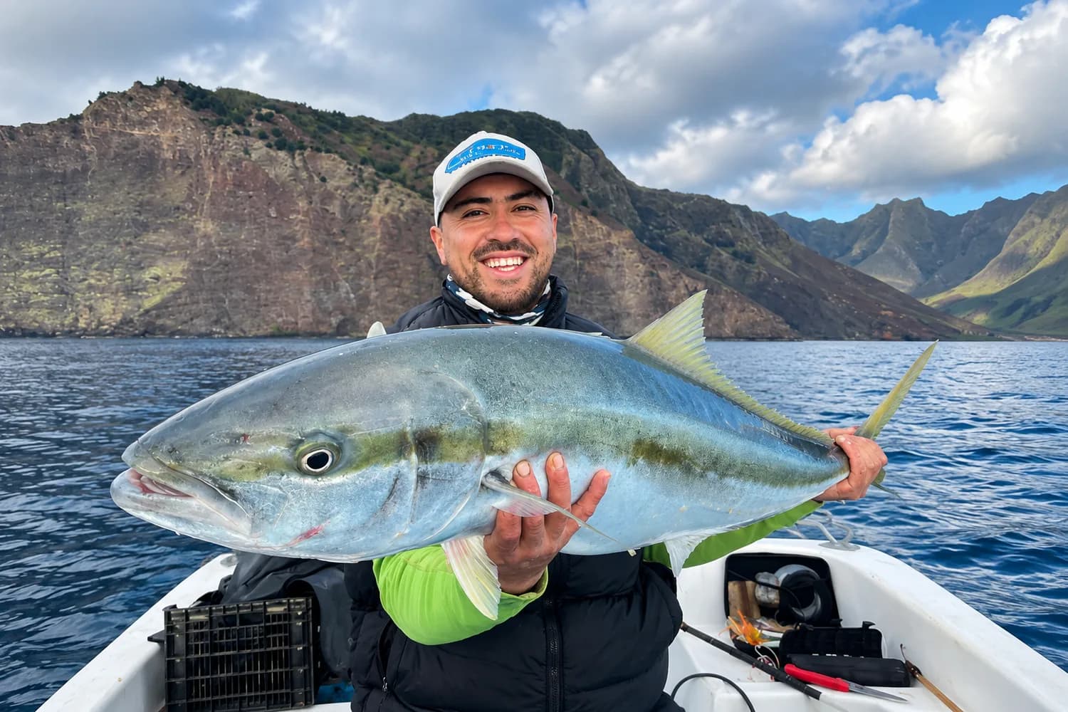 Pescador sosteniendo un ejemplar de gran tamaño a bordo, con los acantilados de Juan Fernández al fondo