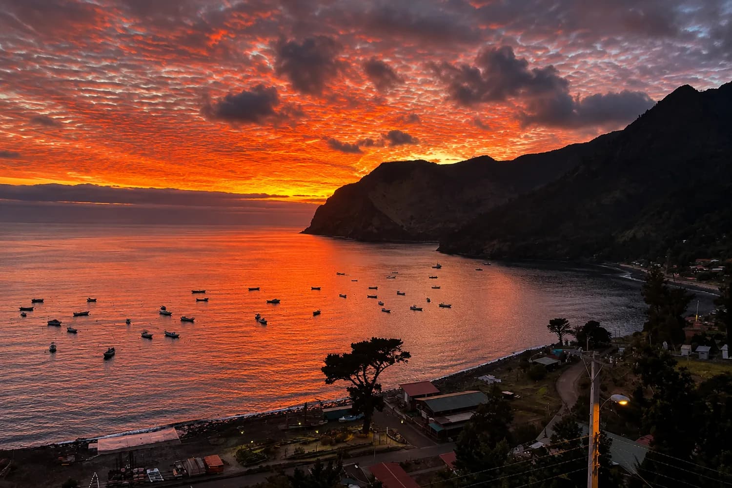 Atardecer de colores intensos sobre Bahía Cumberland, con botes fondeados y el pueblo de San Juan Bautista en la costa